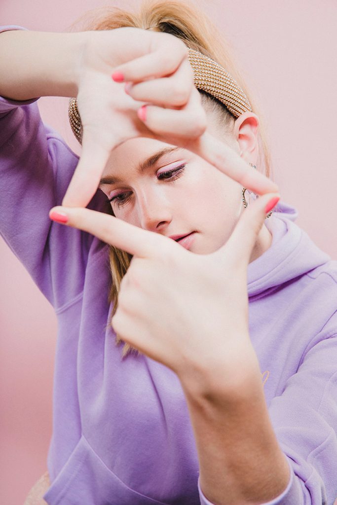 teen wearing purple sweatshirt with pink beauty products on her face
